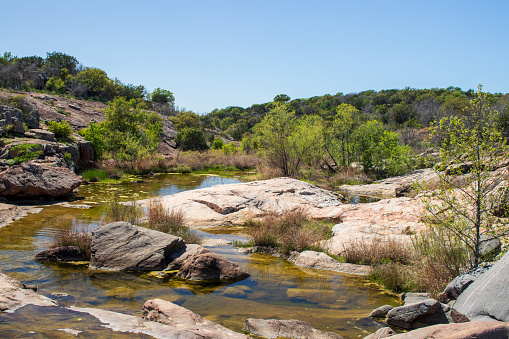 A creek flows over the smooth limestone with the natural beauty of the countryside in this rural Texas Hill Country Park located at Inks Lake State Park, Burnet TX.  The Texas State Parks attract over 9 million visitors a year.