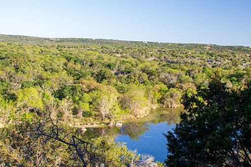 The beautiful colors of Spring in the Central Texas Hill Country with various shades of green trees and reflections in the lake below the valley.  This nature park is located at Inks Lake State Park, Burnet Texas.  People come from everywhere to enjoy camping, kayaking, fishing, and exploring nature and wildlife trails.