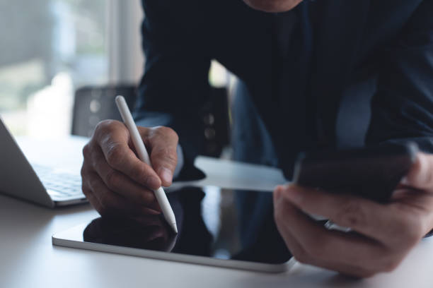 istock Businessman using electronic pencil or stylus pen signing contract on digital tablet via mobile app, using mobile phone with laptop computer on office table 1477989262