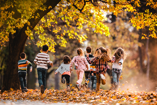 Back view of playful children running in autumn day at the park. Copy space.