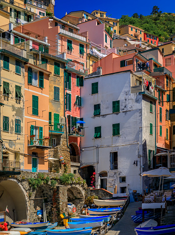 Traditional colorful houses on a hillside street and fishing boats in old town of Riomaggiore in Cinque Terre on the Mediterranean Sea, Italy