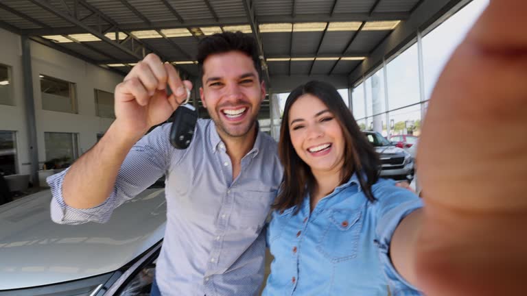 Happy couple on a video call showing to camera the keys to their new car while at the dealership