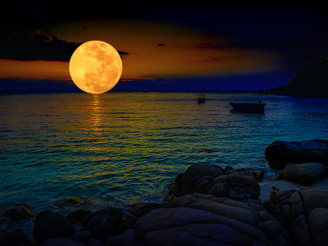 Orange color full moon in the night dark sky with light clouds  above the sea with boats , copy space
