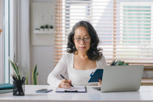 istock Senior stylish entrepreneur wearing eyeglasses, working on a computer, with a notebook and pen at her home office. 1477996425