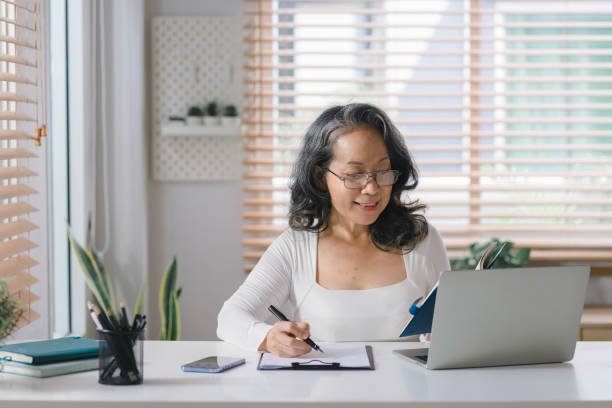 istock Happy senior stylish entrepreneur wearing eyeglasses, working on a computer, with a notebook and pen at her home office. 1477996426