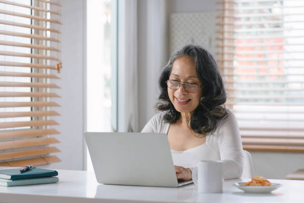 istock At her home office, the senior entrepreneur wears stylish glasses while working on her computer and taking notes with pen and paper. 1477996545