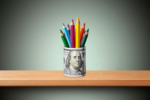 Roll of dollar banknotes with colored pencils on the shelf.