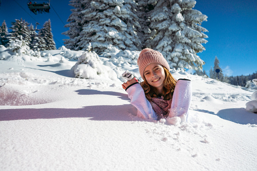 Young cheerful woman is lying in the snow and making snow angel. Person behind a camera helping her to get up. POV concept.