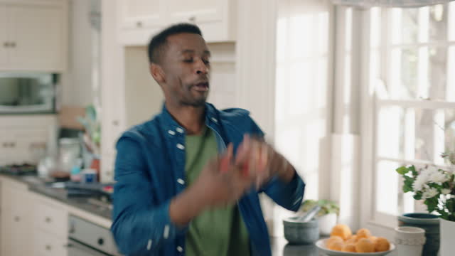 happy african american man dancing in kitchen juggling with apples having fun celebration enjoying weekend at home