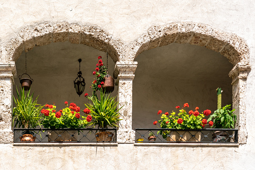 Old small loggia, or covered balcony, arcade with two rounded arches and red geraniums in side street of Italian small town