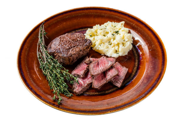 istock Sliced fillet mignon or tenderloin beef steak on a rustic plate with mashed potato.  Isolated on white background. 1478017208