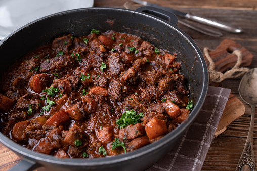 Homemade delicious braised pork dish with carrots, onions, garlic and herbs in a delicious brown gravy. Served ready to eat in a pot on rustic and wooden table background. Closeup