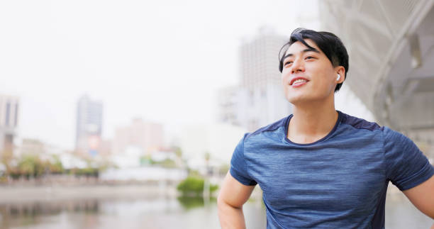 slow motion asian male runner wearing earbuds to listen music is ready to jog in city