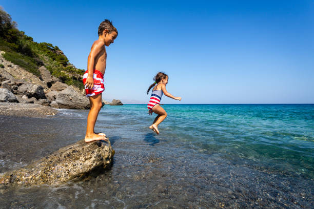 Cheerful children jumping from a cliff in to the sea.
