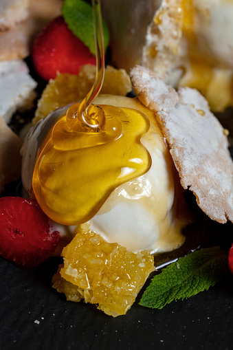 Ice cream balls poured with honey, strawberries, orange, pastries and mint on a plate