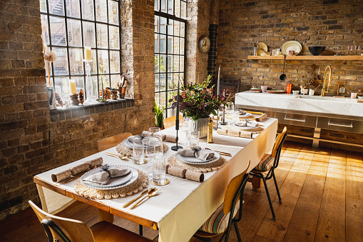 Warm winter light streams through industrial style windows on to a beautifully laid dining table in open plan converted warehouse style apartment