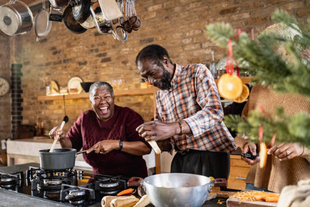 Senior couple joke with each other as they cook together Black male and female in their 60s having fun cooking. He peels winter vegetables while she stirs the pot. typical average stock pictures, royalty-free photos & images