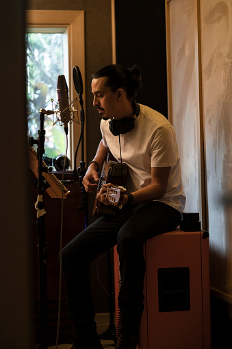 White long haired man writing songs, playing acoustic guitar and composing at a musical recording studio