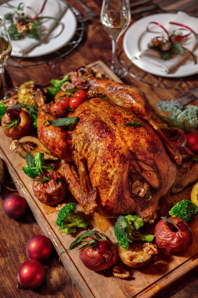 istock Stuffed fried chicken with broccoli, apple, rosemary, walnuts, tomatoes lying on a wooden board surrounded by a festive table, plates, glasses and Christmas tree decorations 1478028603