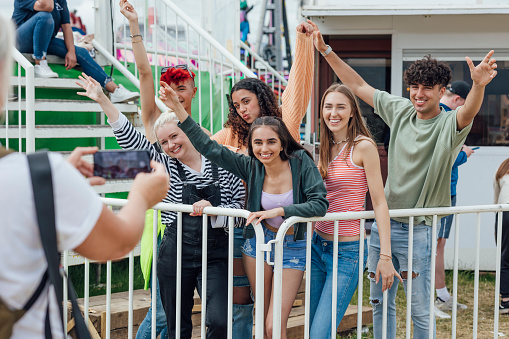 Group of teenagers enjoying a funfair in Newcastle, North East of England. They are standing together posing for a picture an unrecognisable person is taking on a phone while queueing for a ride. One of the models is gender fluid.