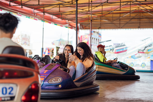 Group of teenagers enjoying a funfair in Newcastle, North East of England. They are on a dodgem ride laughing and having fun. One of the teens is holding a mobile phone.
