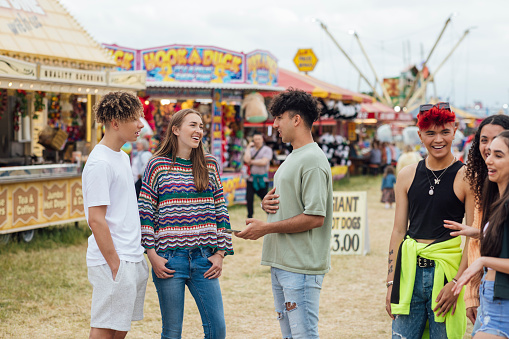 Group of teenagers enjoying a funfair in Newcastle, North East of England. They are  standing in a field filled with stalls and rides, laughing and talking together. One of the models is gender fluid.