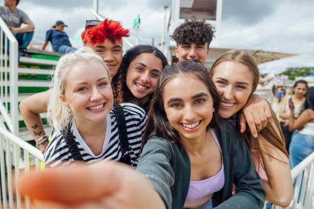 Group of teenagers enjoying a funfair in Newcastle, North East of England. They are standing together smiling looking at the camera while queueing for a ride. One of the models is gender fluid.