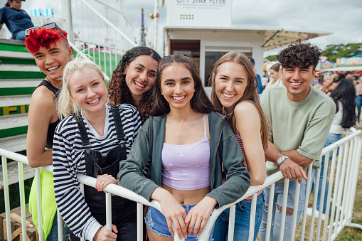 Group of teenagers enjoying a funfair in Newcastle, North East of England. They are standing together smiling looking at the camera while queueing for a ride. One of the models is gender fluid.