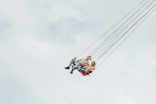 Low angle view teenage friends enjoying a funfair in Newcastle, North East of England. They are on a swing ride laughing and having fun.