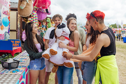 Group of teenagers enjoying a funfair in Newcastle, North East of England. They are laughing and cheering together a one of the girls has just won a prize at a stall. One of the models is gender fluid.