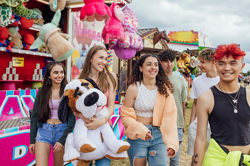 Group of teenagers enjoying a funfair in Newcastle, North East of England. They are laughing and one of the girls has just won a prize at a stall, holding it as they walk. One of the models is gender fluid.