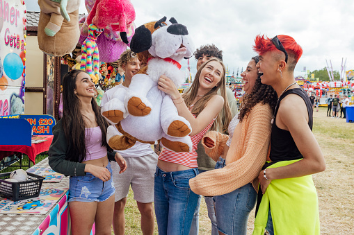 Group of teenagers enjoying a funfair in Newcastle, North East of England. They are laughing and cheering together a one of the girls has just won a prize at a stall. One of the models is gender fluid.