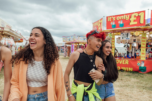 Group of teenagers enjoying a funfair in Newcastle, North East of England. They are walking through a field filled with stalls and rides, laughing and talking together. One of the models is gender fluid.