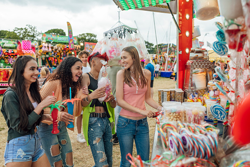 Group of teenagers enjoying a funfair in Newcastle, North East of England. They are buying sweet foods from a stall together. One of the models is gender fluid.