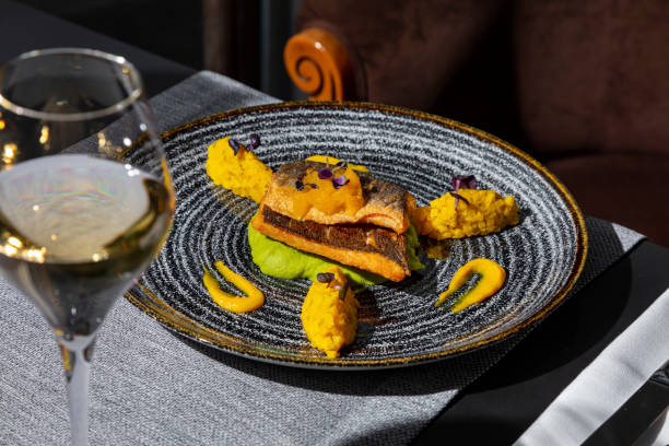istock Fried fish with mashed potatoes, sprouts, mango, and sauce in a plate on the table with a napkin, cutlery and a glass of wine 1478031151