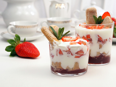 Strawberry dessert with mascarpone and whipped cream, savoiardi biscuit and fresh strawberry in a glass on white background. Recipe of simple dessert, or berry trifle cake.