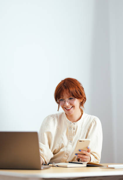 Smiling Young Woman Using Laptop Computer And Mobile Phone At Home
