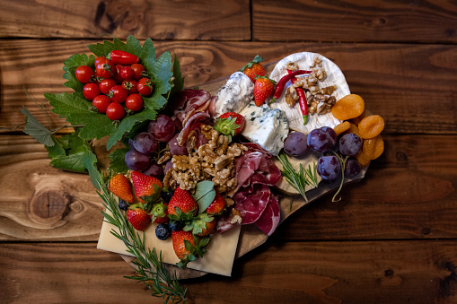 An aerial view of a freshly prepared sharing appetizer board on a wooden dining table. It is made up of deli meats and homegrown organic local produce from Toulouse in the south of France.