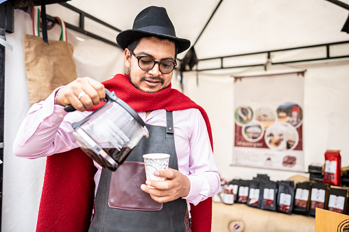 Mid adult man serving your own coffee on a disposable cup to a customer at market stall