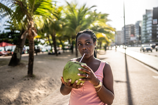 Mid adult woman drinking coconut water and looking around in a beach boardwalk