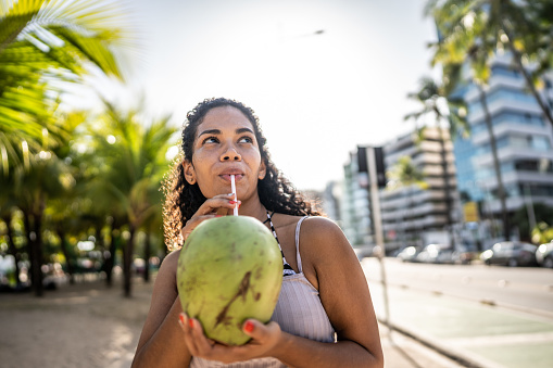 Mid adult woman drinking coconut water and looking around in a beach boardwalk