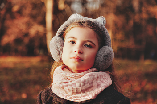 Face pensive little girl child model in coat posing in autumn sunlight park, looking at camera. Sad cute lady kid in fall nature leisure activity. Childhood vitality concept. Copy text space for ad