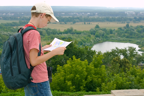 Boy with binoculars and backpack looks at the map on a hike