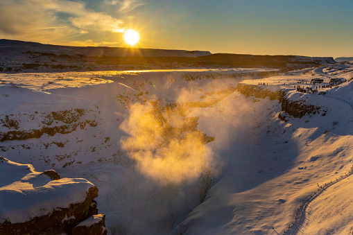The double waterfall of Gullfoss formed by the rupture of the tectonic plates illuminated by the first rays of the dawn sun illuminating the mist that emanates from the river. Silhouettes of tourists