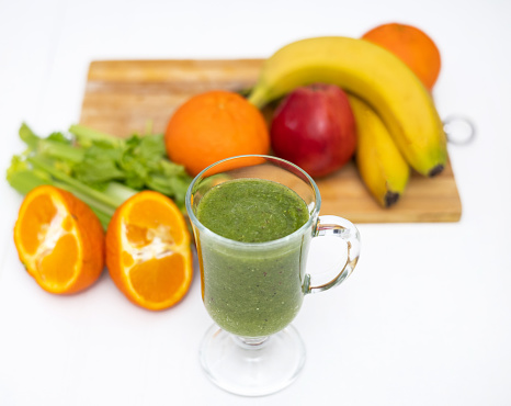 slim woman doing healthy smoothie at kitchen from celery apple kiwi and tangerine fruit.millennial female pressing blender button, drinking or sitting with cup in front of belly.postpartum recovery