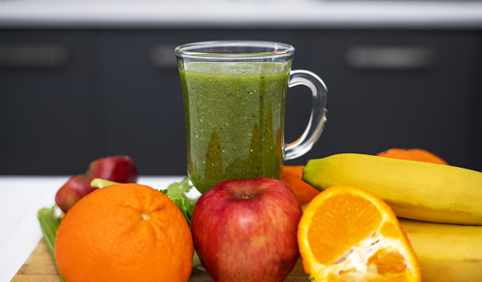 slim woman doing healthy smoothie at kitchen from celery apple kiwi and tangerine fruit.millennial female pressing blender button, drinking or sitting with cup in front of belly.postpartum recovery