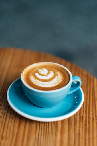 Top view of blue cup of tasty cappuccino with latte art on wooden table background