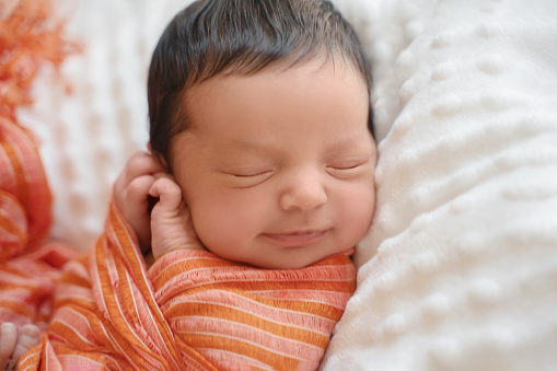 Bebé recién nacido con cabello oscuro sonriendo acostado de lado durmiendo. Lindo niño del Medio Oriente en una manta. Escena tranquila de cerca photo
