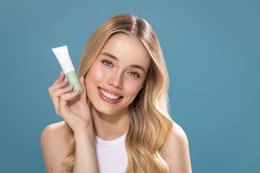 Studio shot of a beautiful natural blonde woman with perfect skin, holding cosmetic jar.