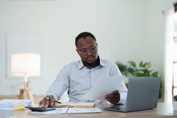 istock middle age man American African using calculator for calculating and laptop computer with planning working on financial document, tax, exchange, accounting and Financial advisor 1478060187